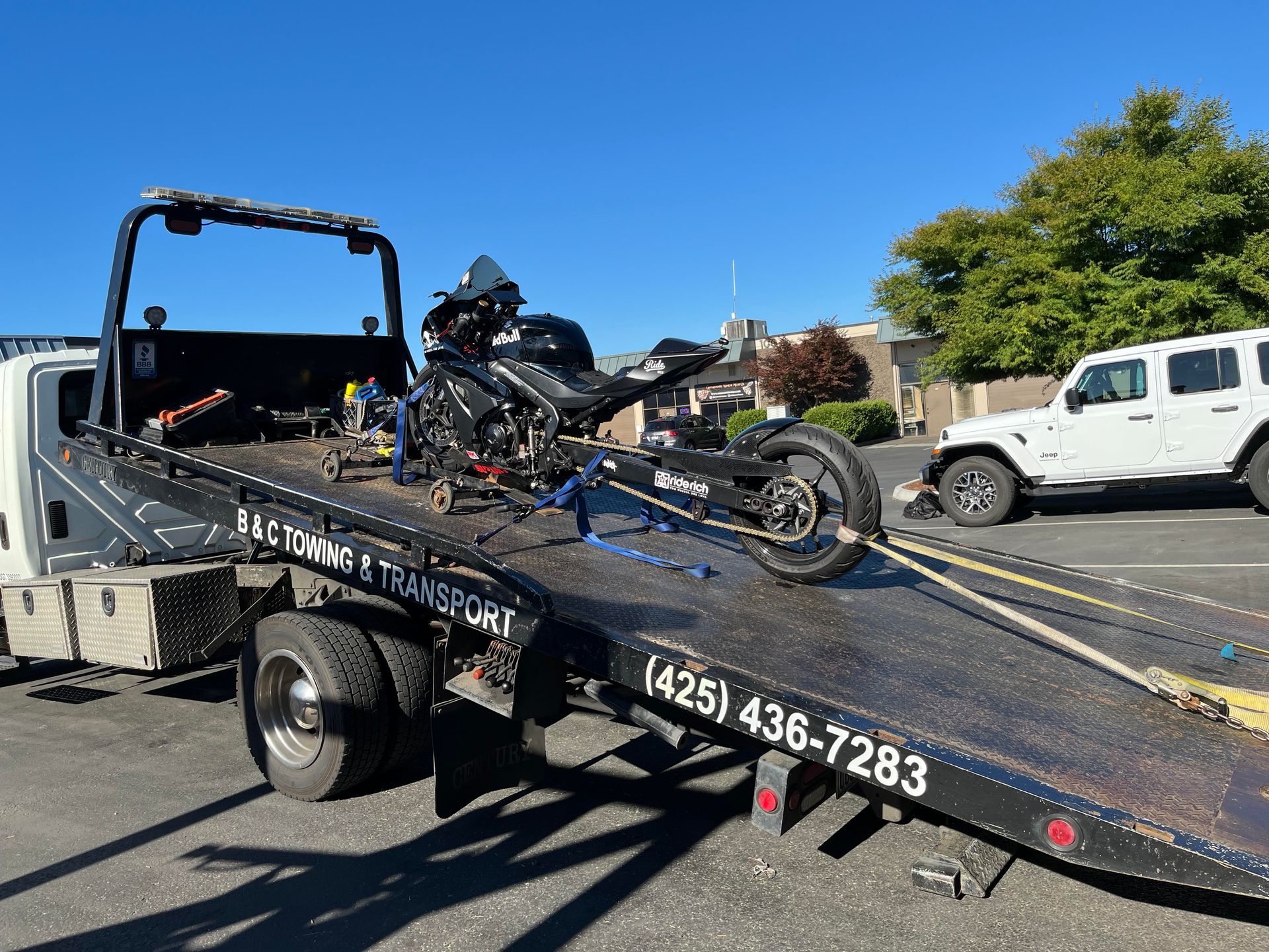 Tow truck loading a black motorcycle on a flatbed in a sunny residential street