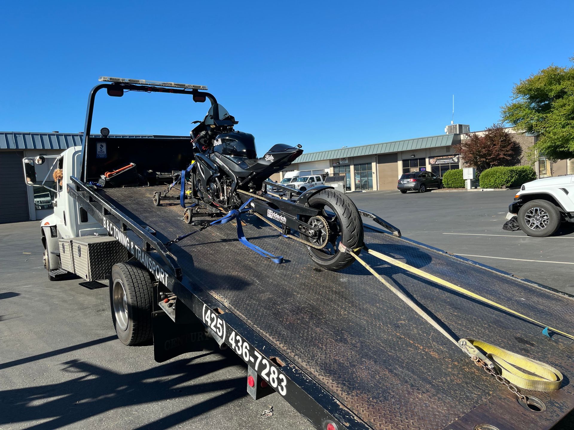 Tow truck hauling a motorcycle on a flatbed ramp along a sunny street