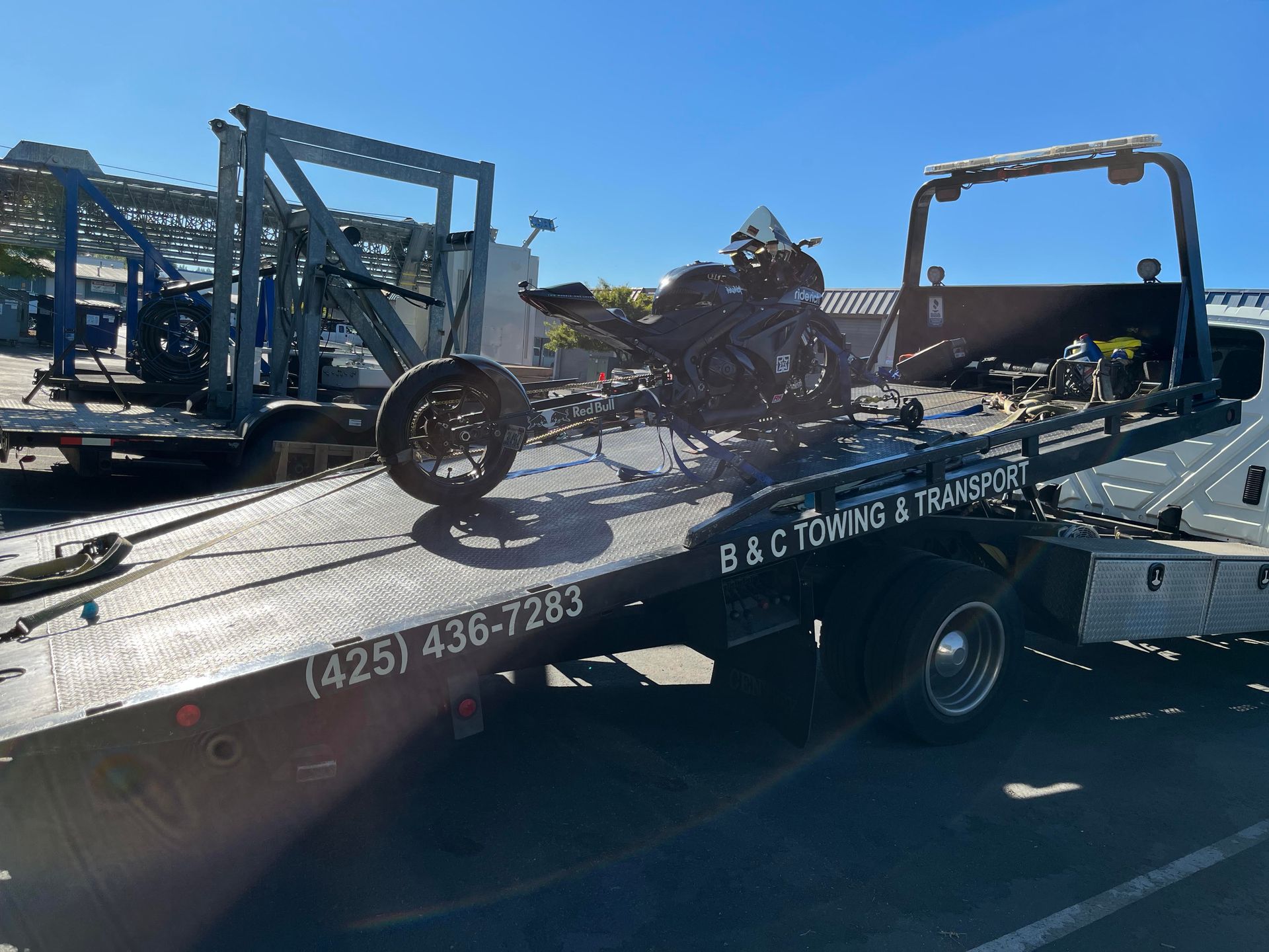 Two motorcycles loaded on a flatbed tow truck, with another truck in the background.