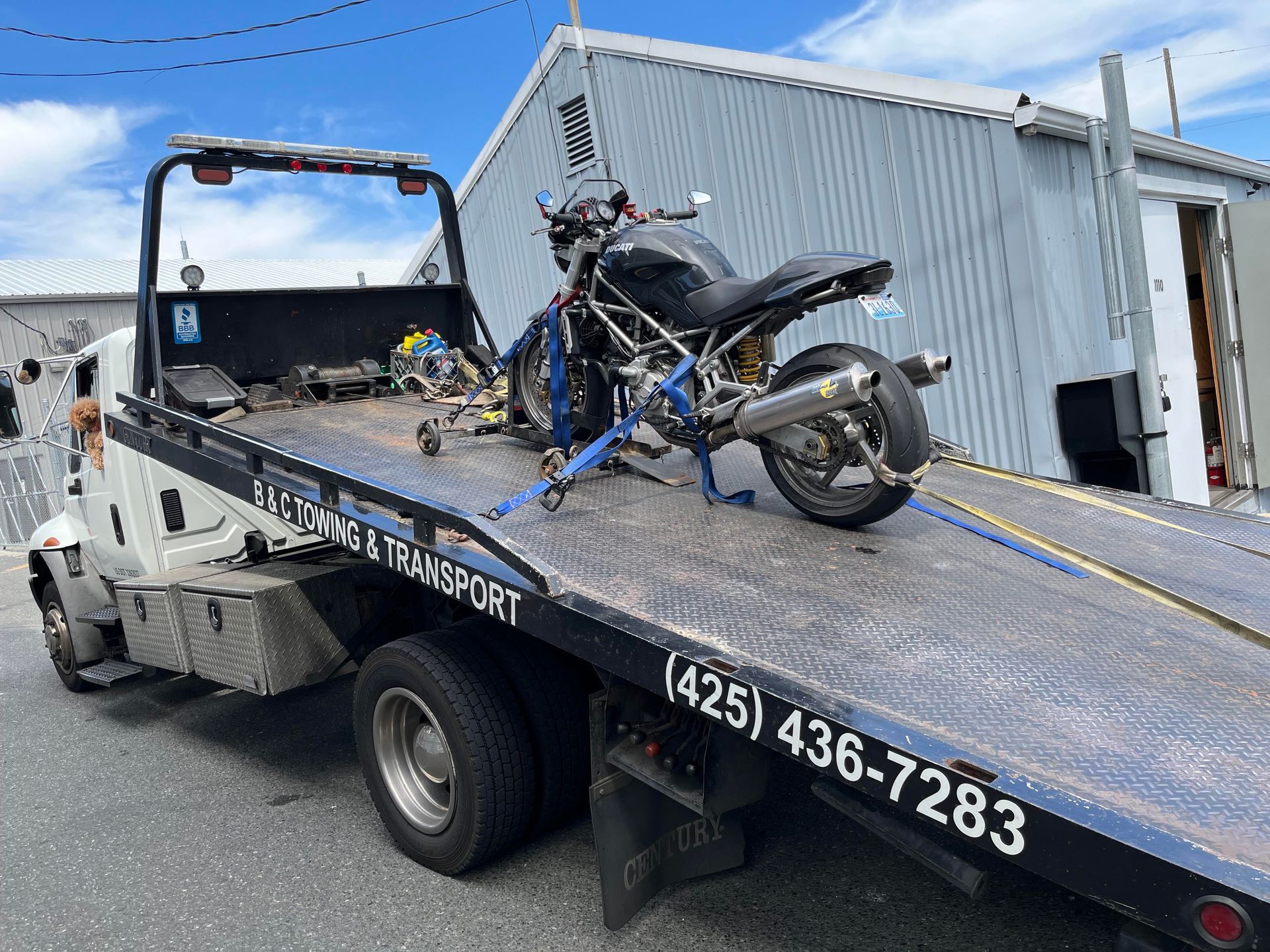 Motorcycle secured on a flatbed tow truck outside a metal building under a blue sky