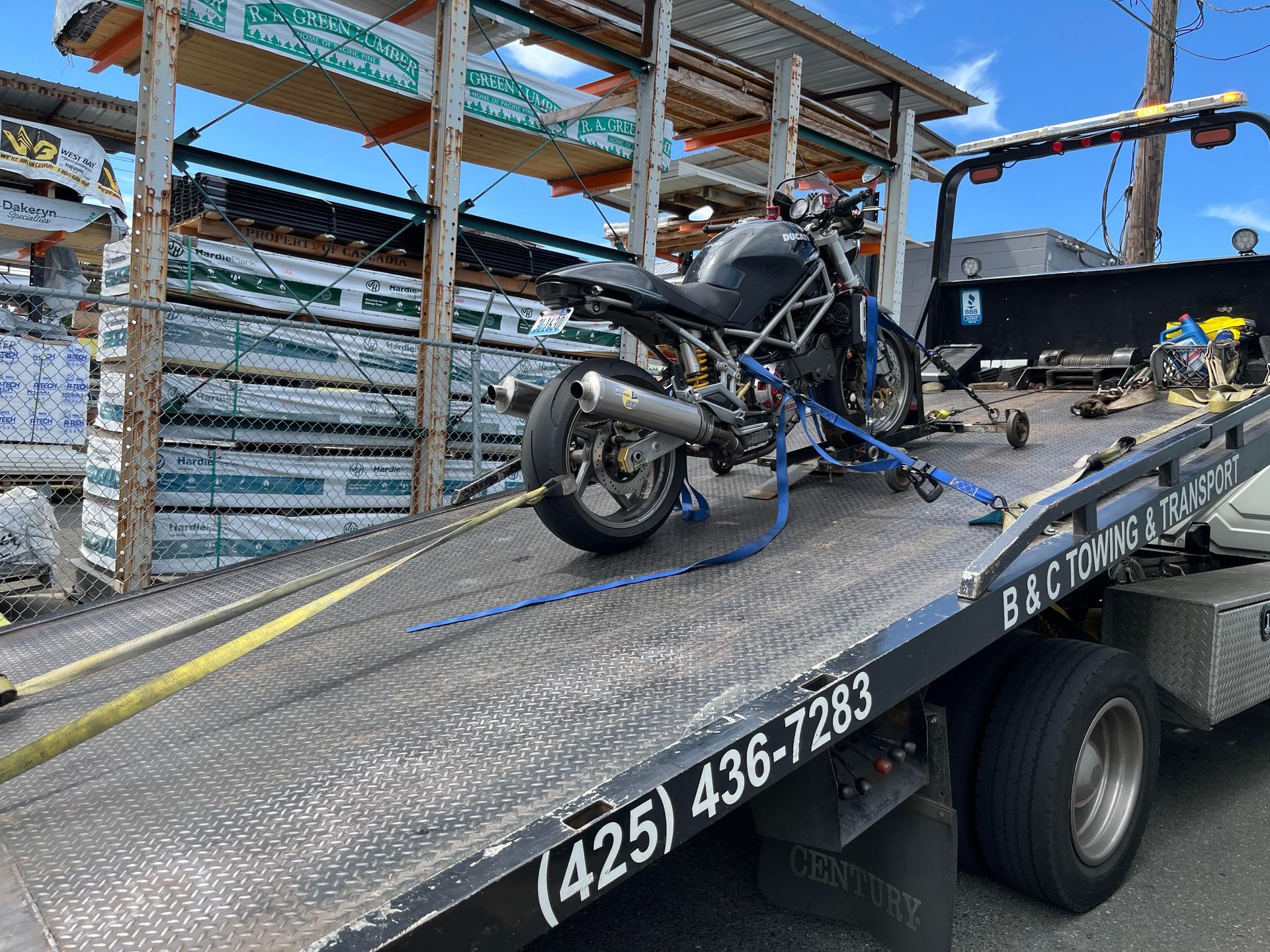Motorcycle strapped on a tow truck flatbed beside stacked wooden pallets and debris