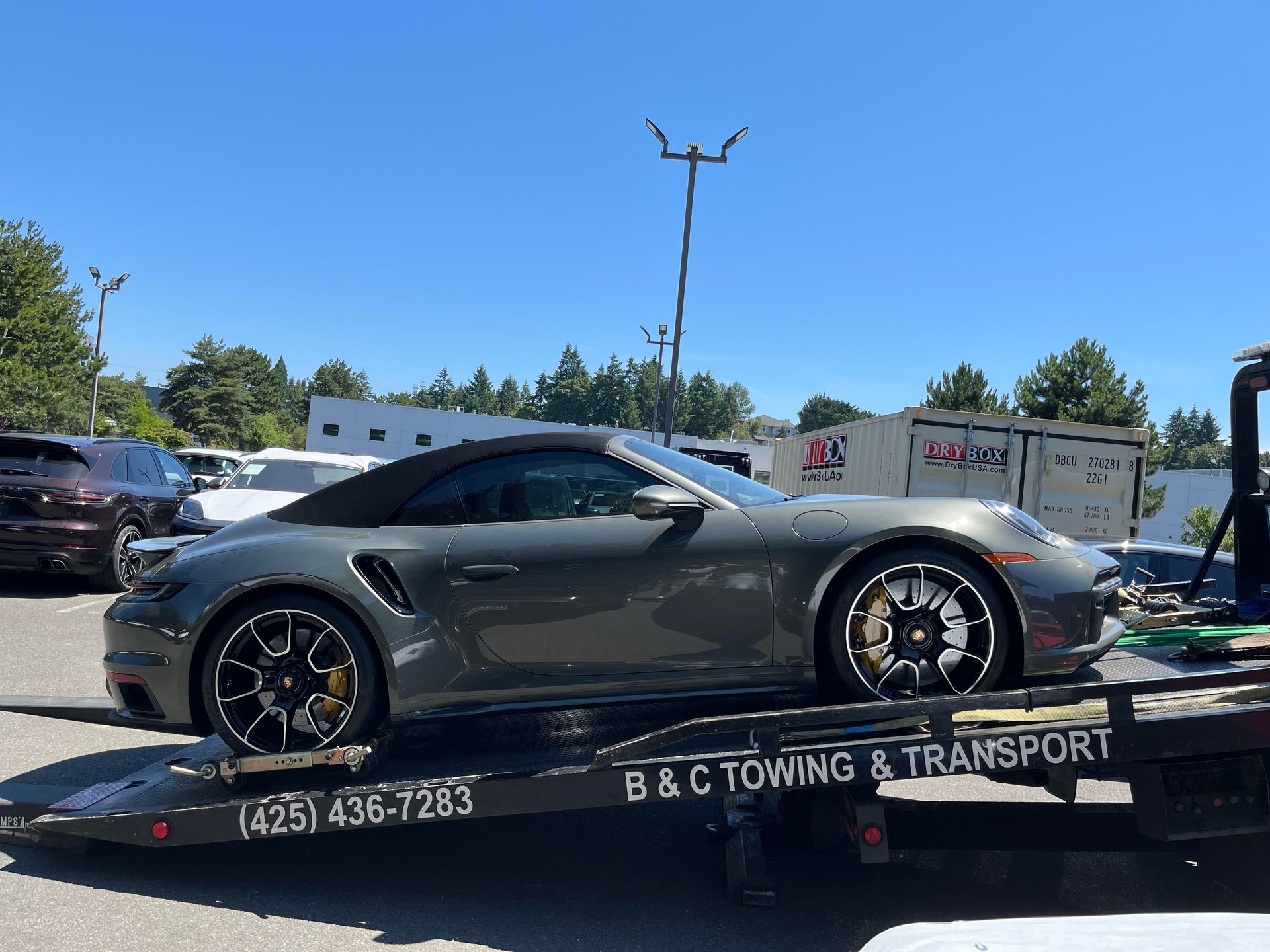 Gray sports car on a flatbed tow truck in a sunny parking lot