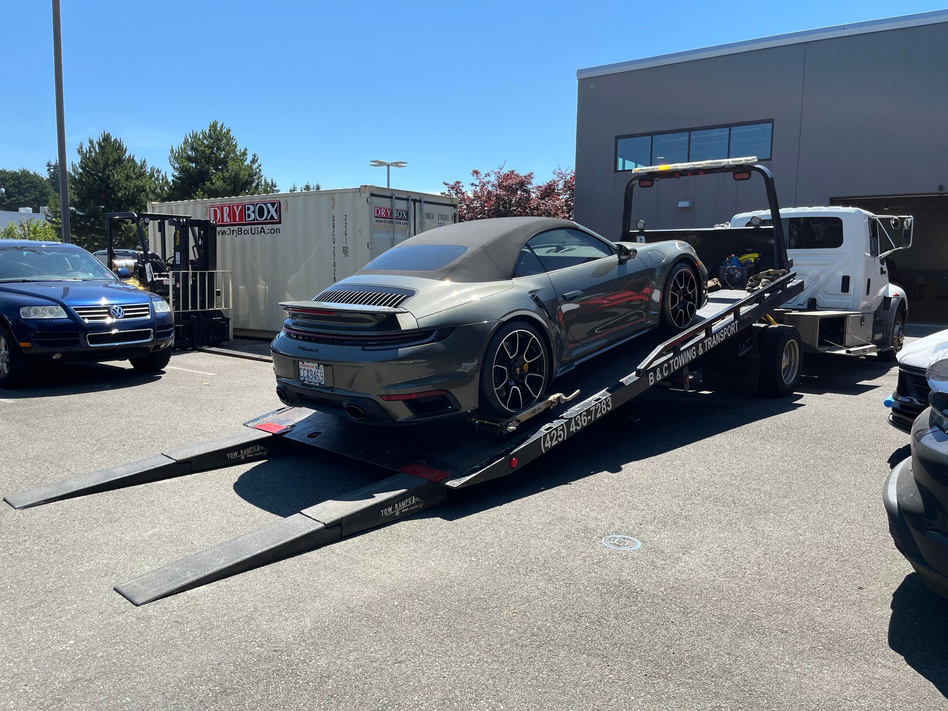 Silver sports car on a tow truck ramp in a sunny parking lot, with other vehicles nearby