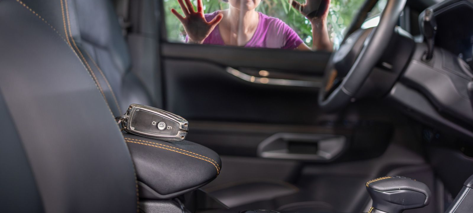 Car interior with black leather seats and a purse on the center armrest, view through the side window
