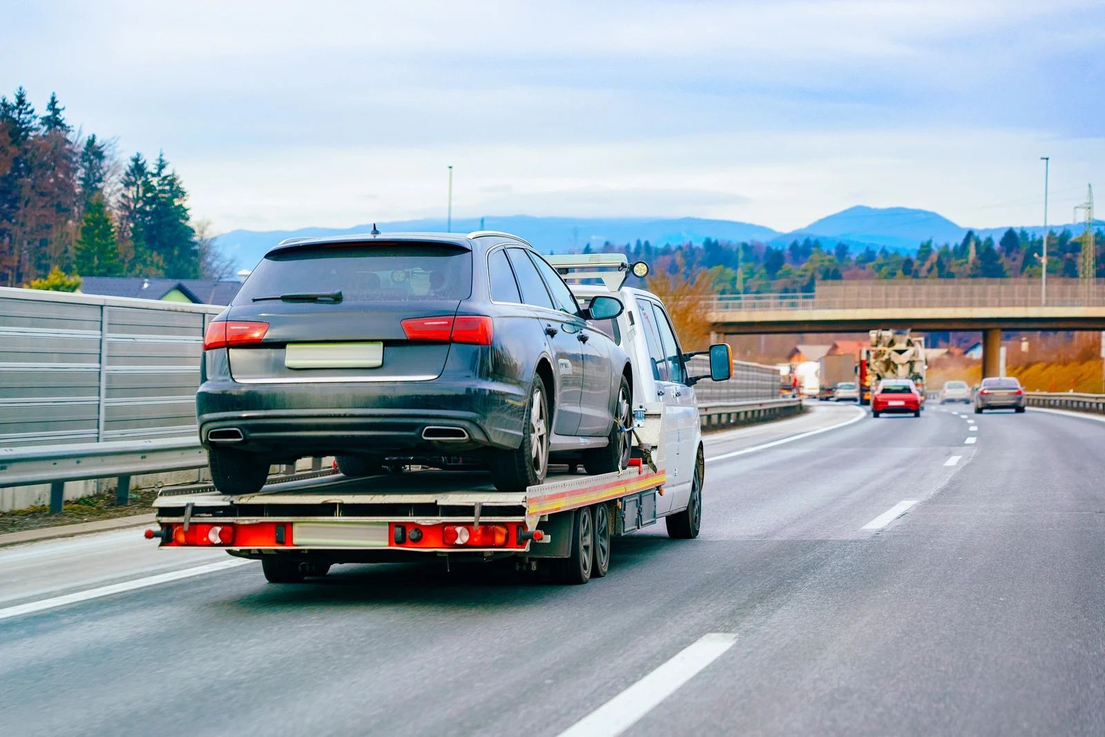 SUV on a flatbed tow truck driving on a highway under an overpass.