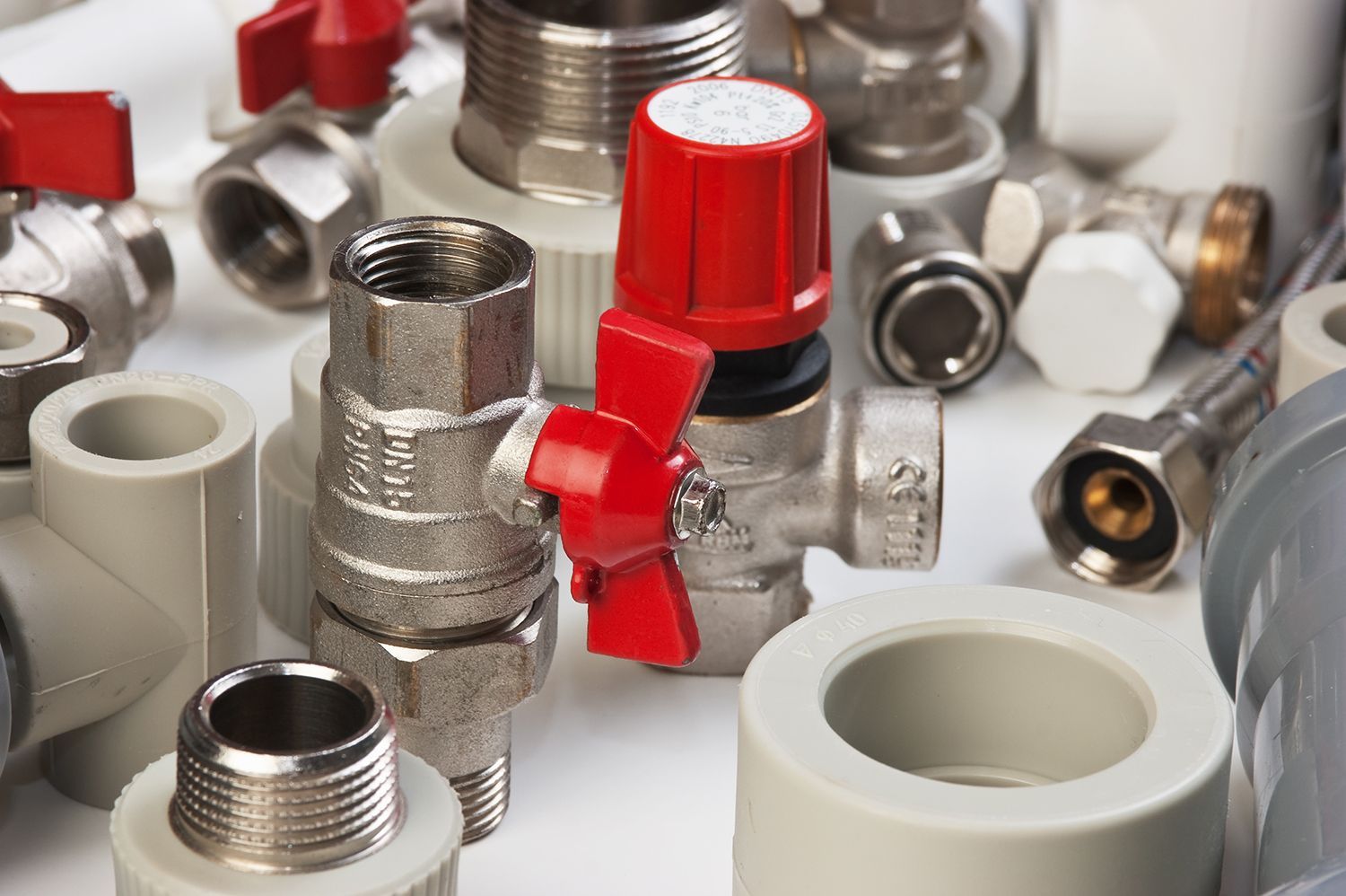 Assorted metal and plastic pipe fittings with red valve caps on a white surface Assorted metal and plastic pipe fittings with red valve caps on a white surface