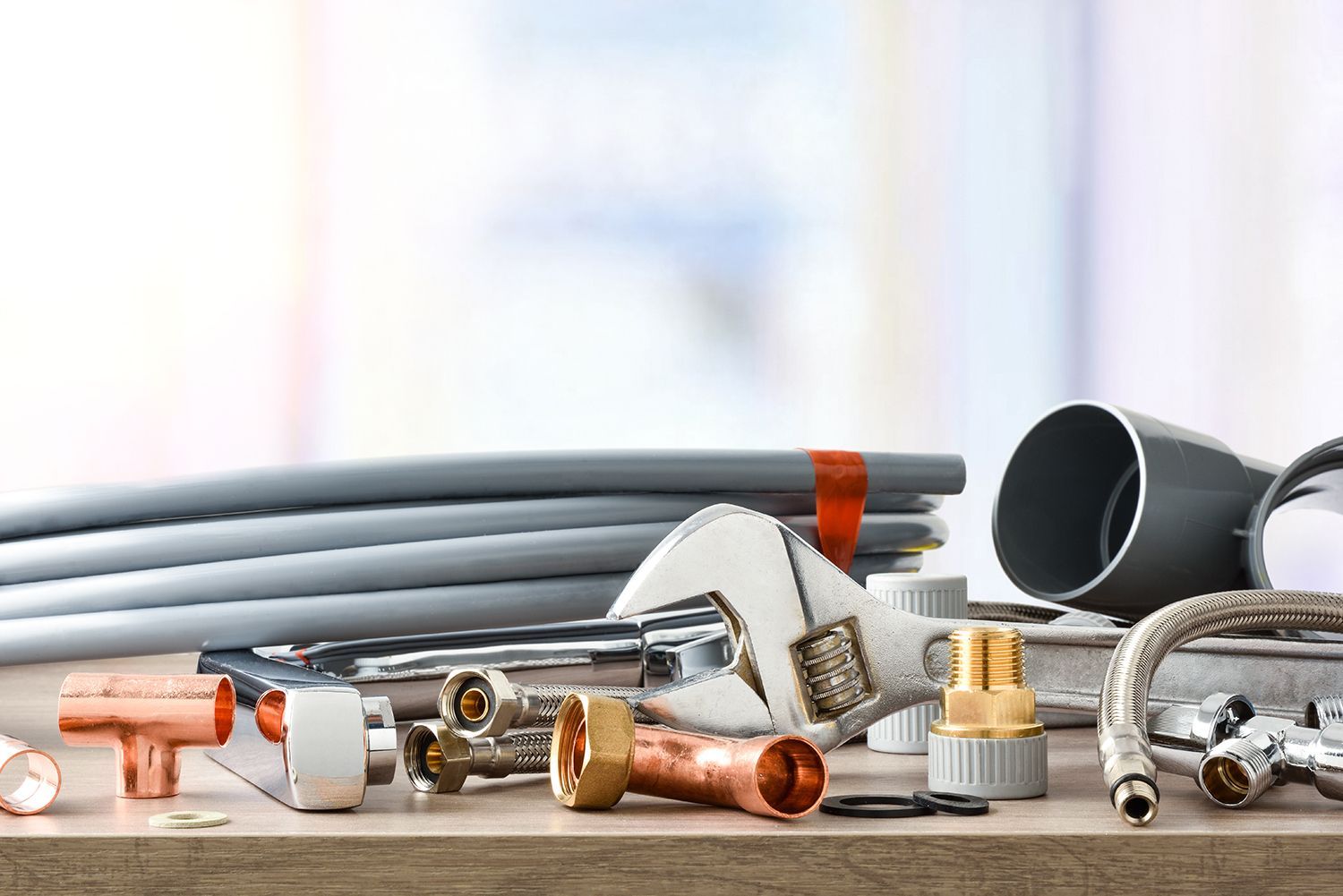 Assorted plumbing pipes, copper fittings, and hose parts on a tabletop with gray tubing in the background Assorted plumbing pipes, copper fittings, and hose parts on a tabletop with gray tubing in the background