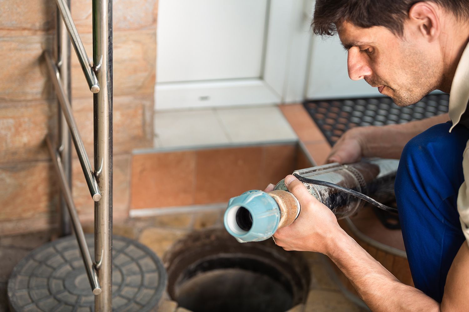 Plumber kneels by a floor drain, inspecting a blue pipe fitting with a flashlight. Plumber kneels by a floor drain, inspecting a blue pipe fitting with a flashlight.