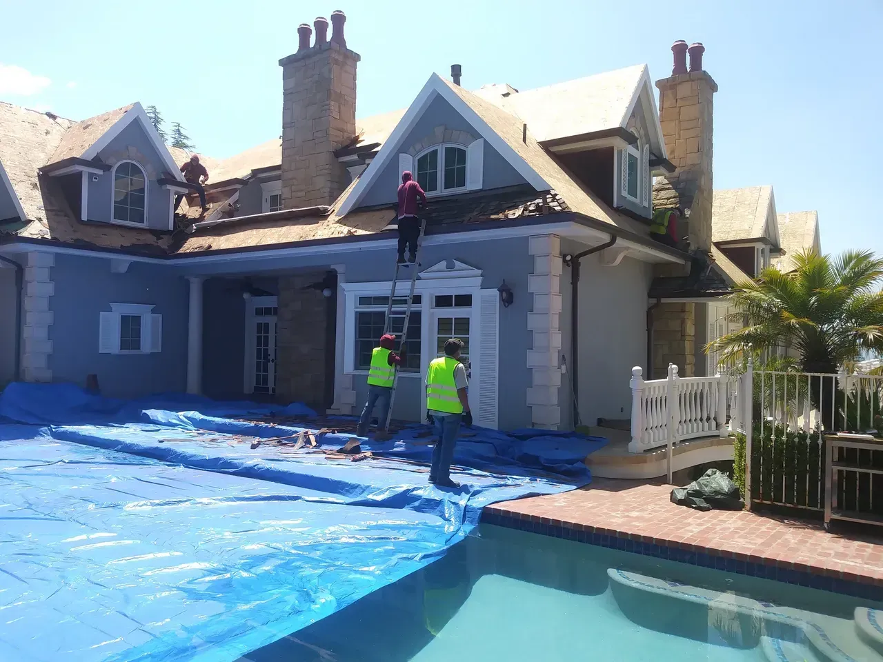 Workers on a house roof under construction, covering the pool with blue tarps.