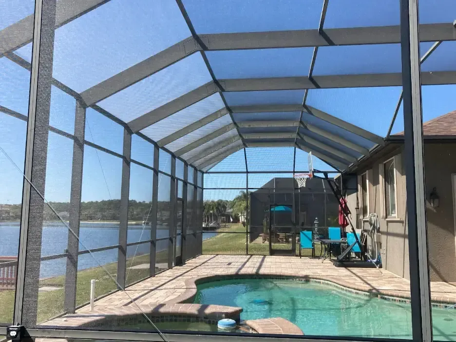 Screened pool enclosure beside a canal, with a small backyard patio and turquoise chairs