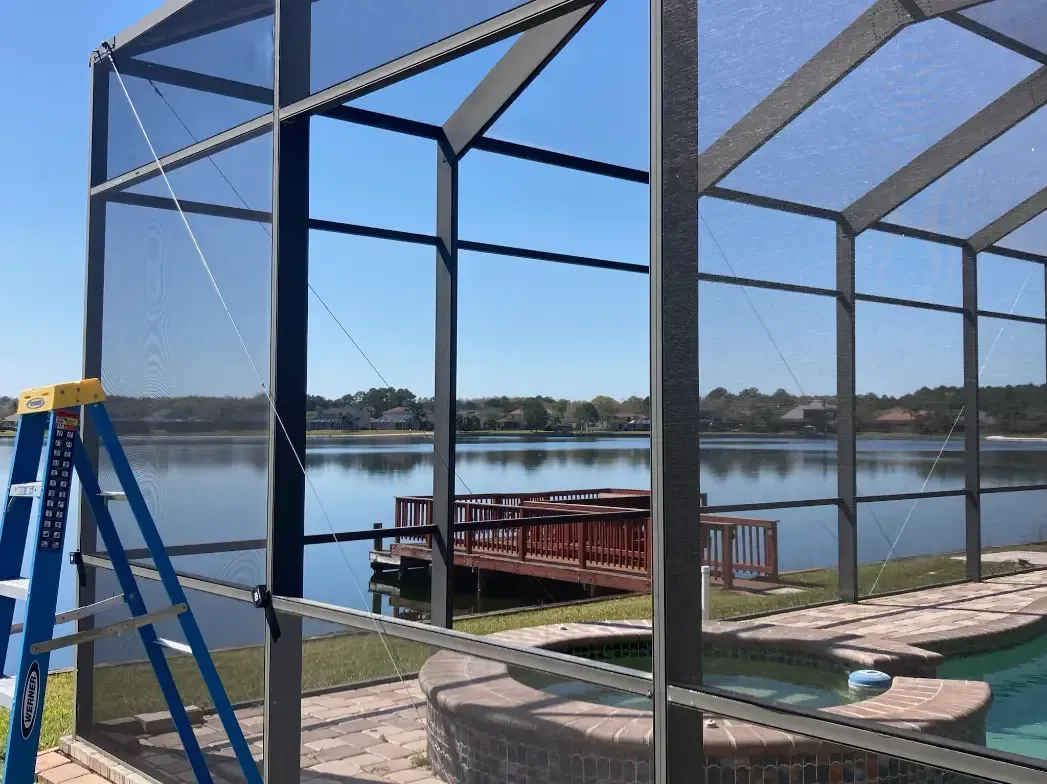 Screened patio under construction beside a lake, with a blue ladder and dock in the background.