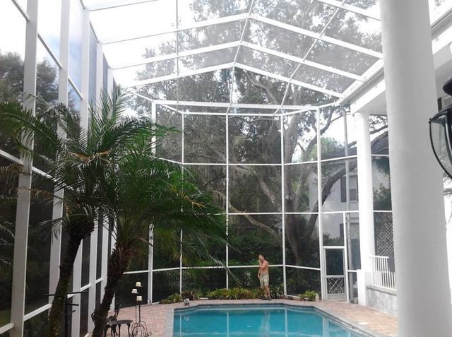 A man is standing next to a swimming pool in a screened in area