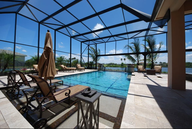 A large screened in swimming pool with chairs and umbrellas