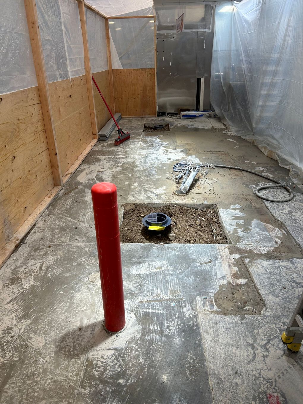 Renovation in progress. Room with plywood, concrete floor, plumbing access, and red pipe.