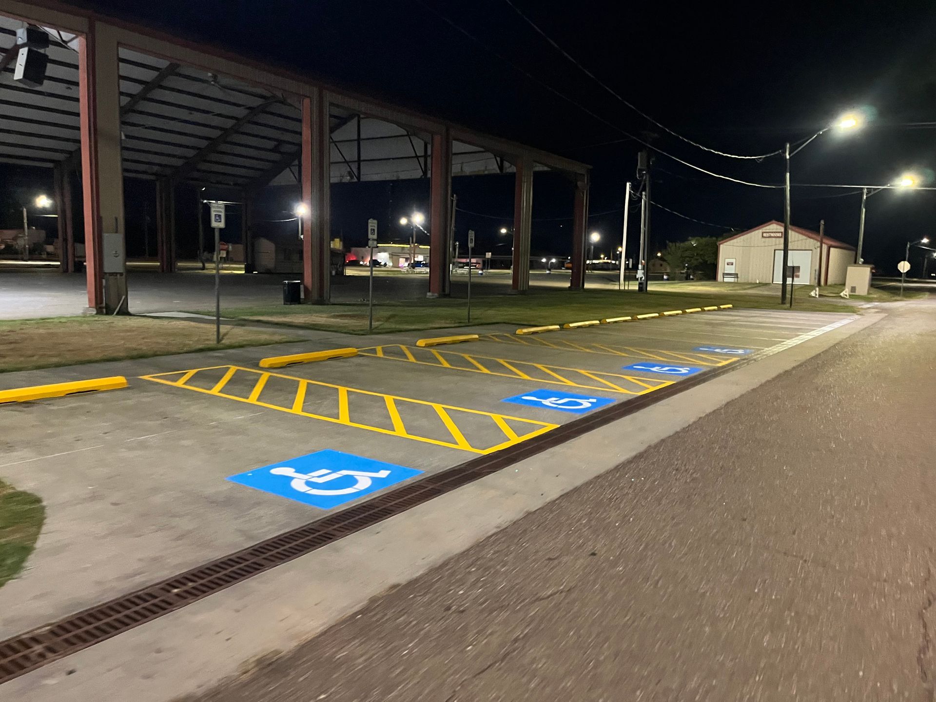 Accessible parking spaces at a covered lot at night, with blue wheelchair symbols and yellow striped access aisles