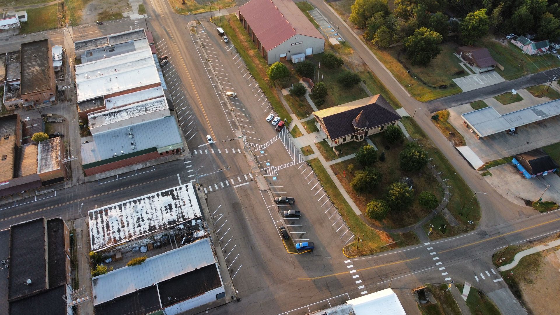 Aerial view of a city street intersection with cars, buildings, and trees at sunset.