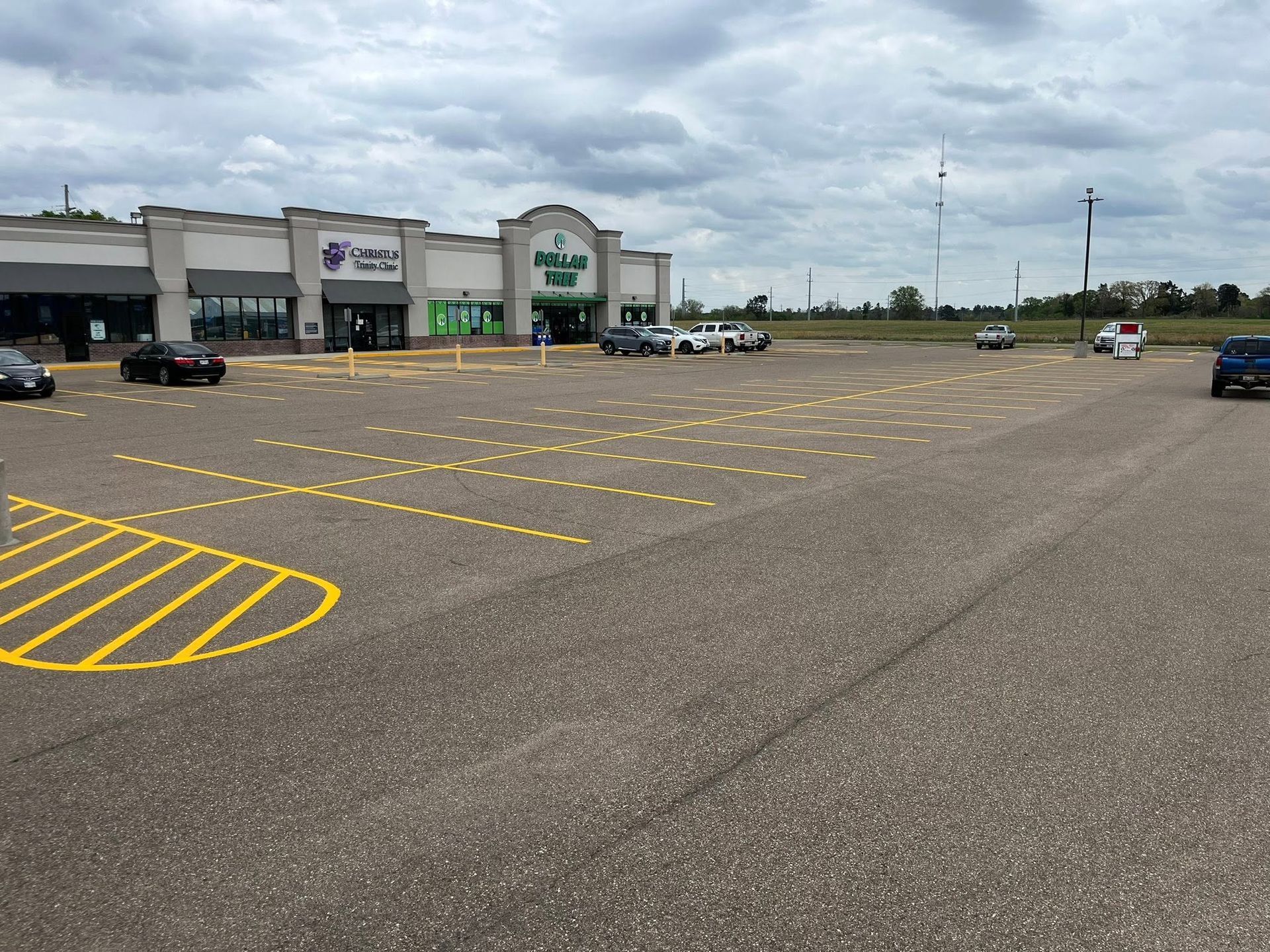 Mostly empty store parking lot with yellow striped accessible spaces under a cloudy sky