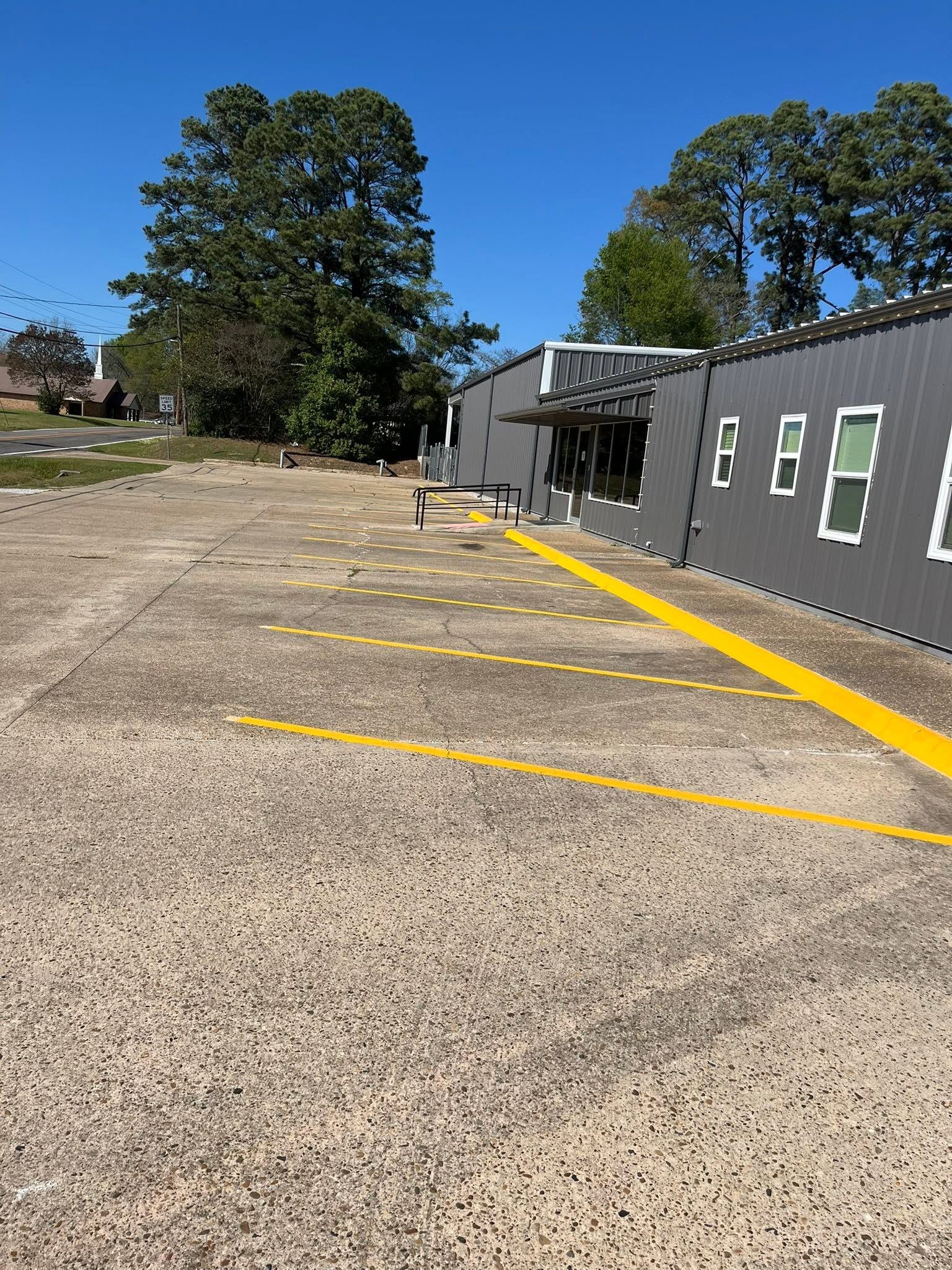 Gravel parking area beside a gray building with yellow lines and trees under a clear blue sky
