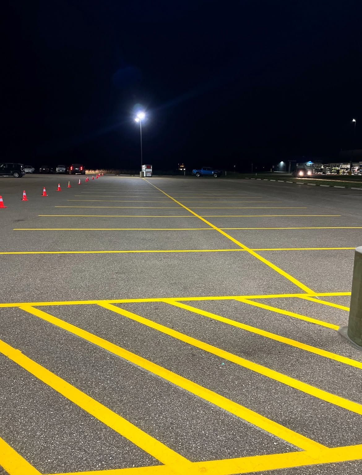 Empty parking lot at night, lit by a bright pole light with yellow striped pavement markings and cones.