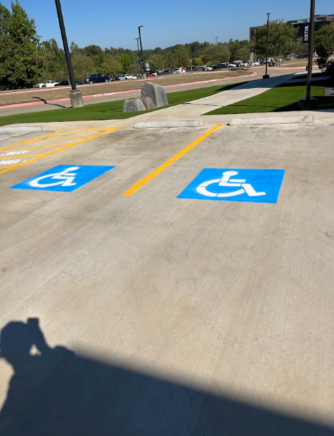 Accessible parking spaces with blue wheelchair symbols painted on pavement near a sidewalk.