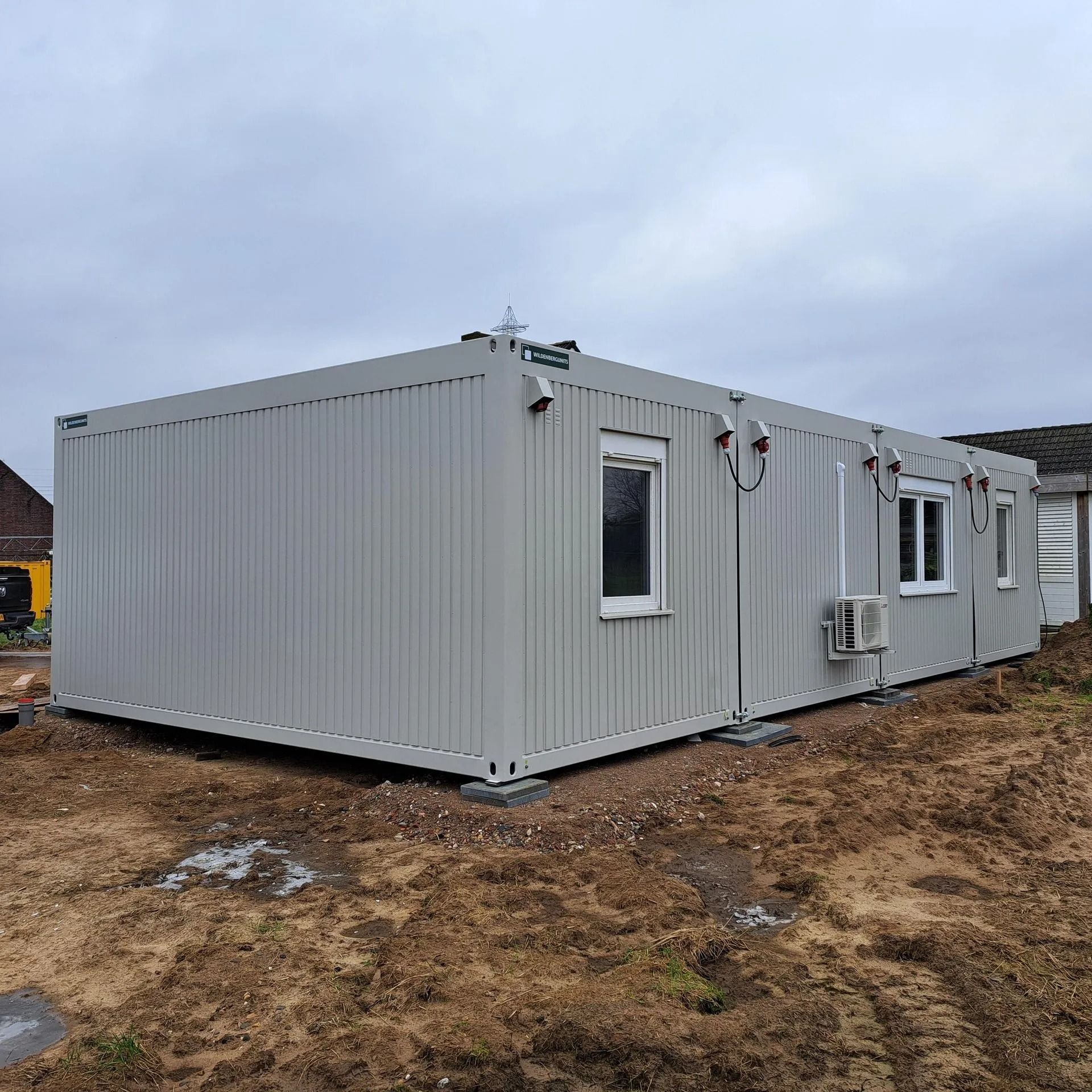 Een grijs gebouw met rode randen en een bordje met daarop 'a'