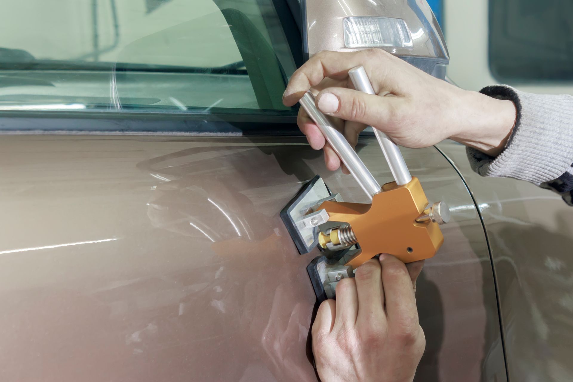 Paintless dent repair removing a car door dent with a dent puller tool.