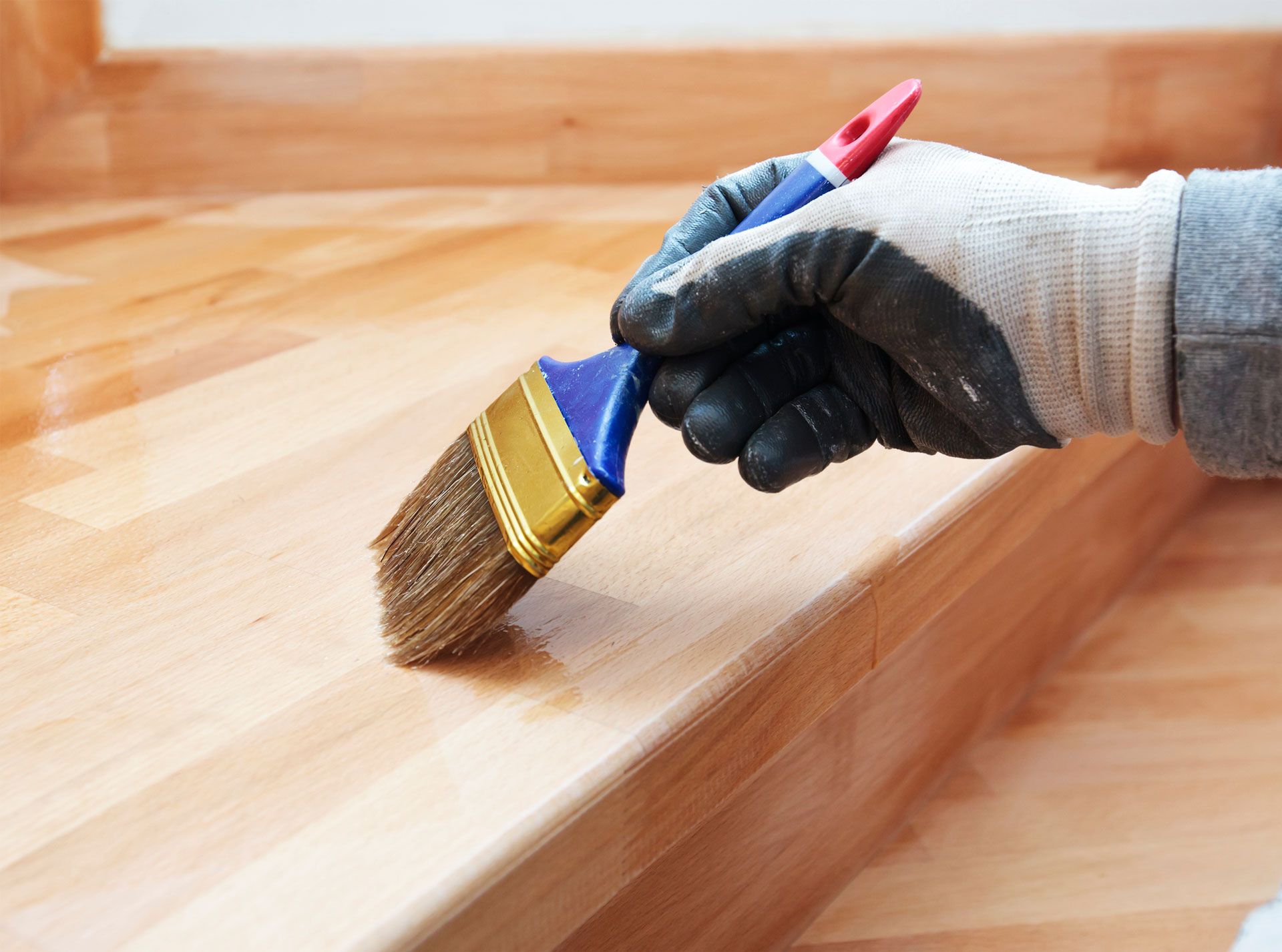 Person wearing a glove applying stain with a brush to a wooden surface.