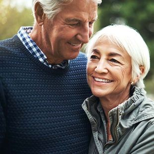 Smiling older couple outdoors, standing close together in sweaters and jackets