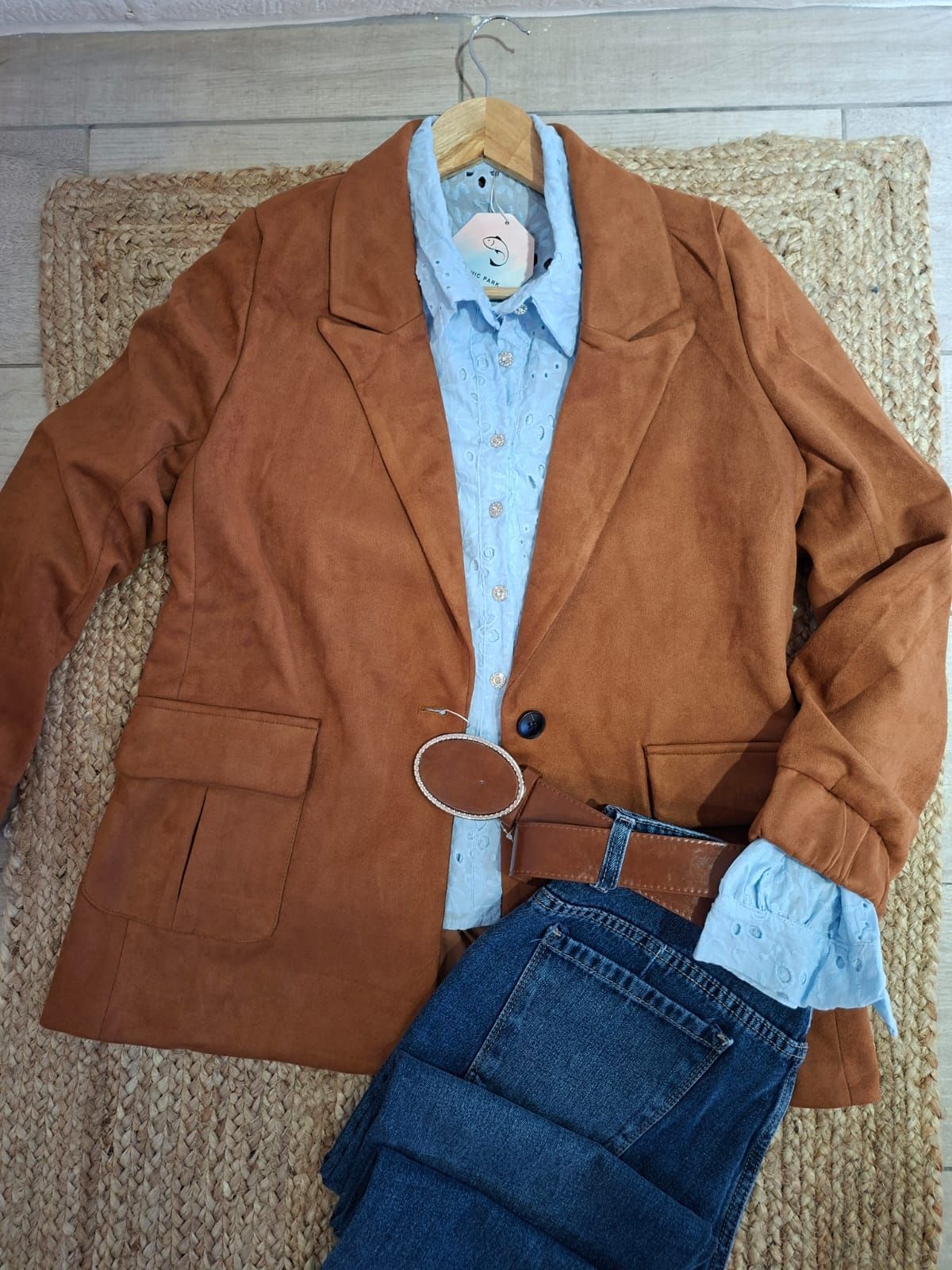 Un blazer color óxido, una camisa azul claro y unos vaqueros oscuros extendidos sobre una alfombra tejida.