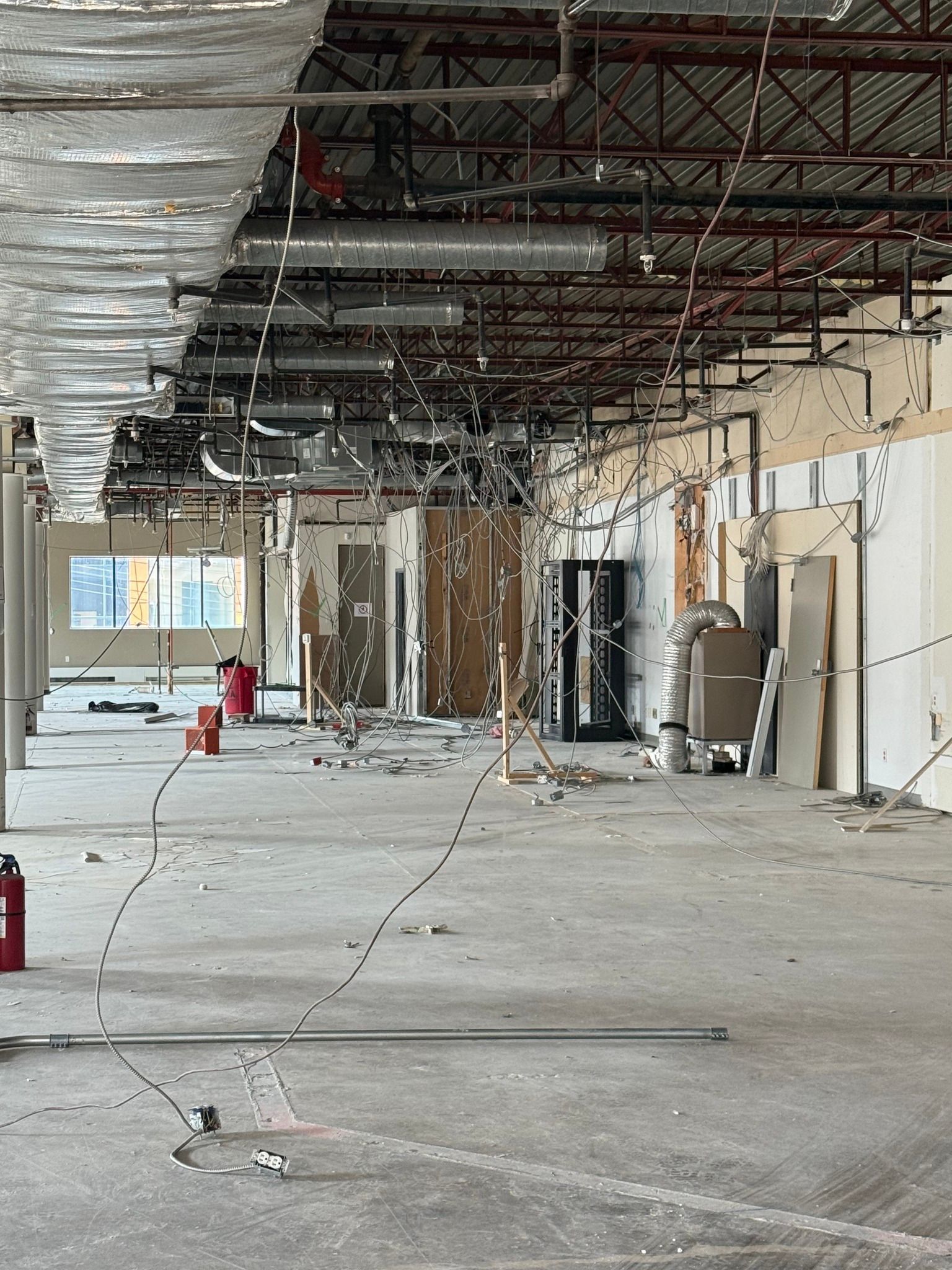 Un grand espace commercial inachevé, en cours de rénovation intérieure, avec des poutres de plafond apparentes et des sols recouverts de débris.