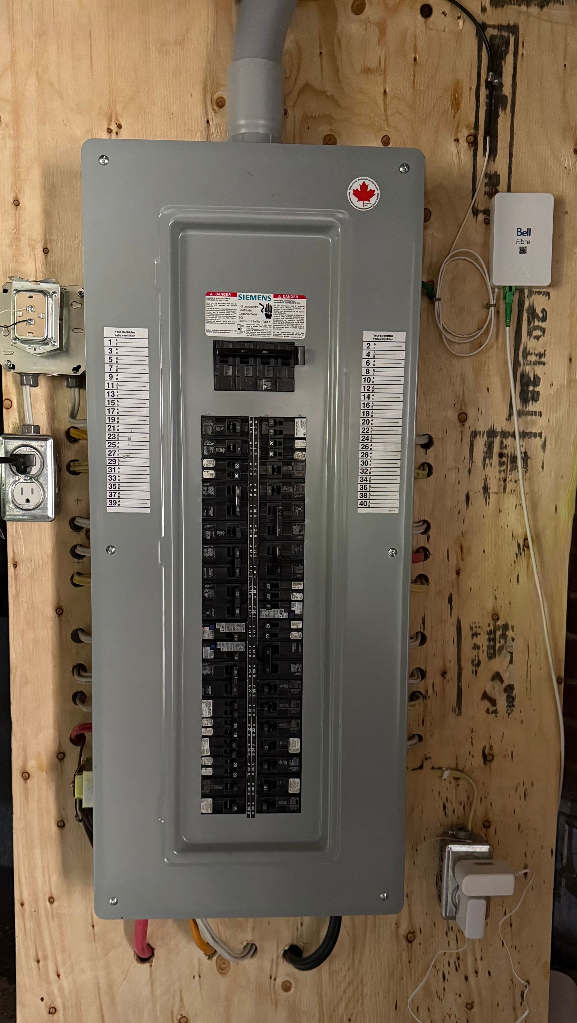 A gray electrical breaker panel mounted on a plywood wall in a utility setting.