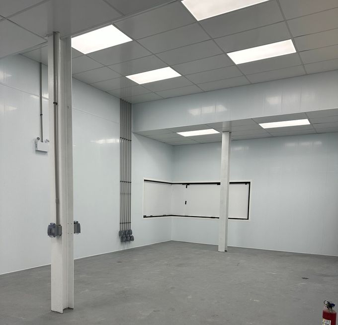 Pièce moderne et vide, avec des murs lambrissés blancs, un sol gris, des spots encastrés au plafond et deux colonnes de soutien.