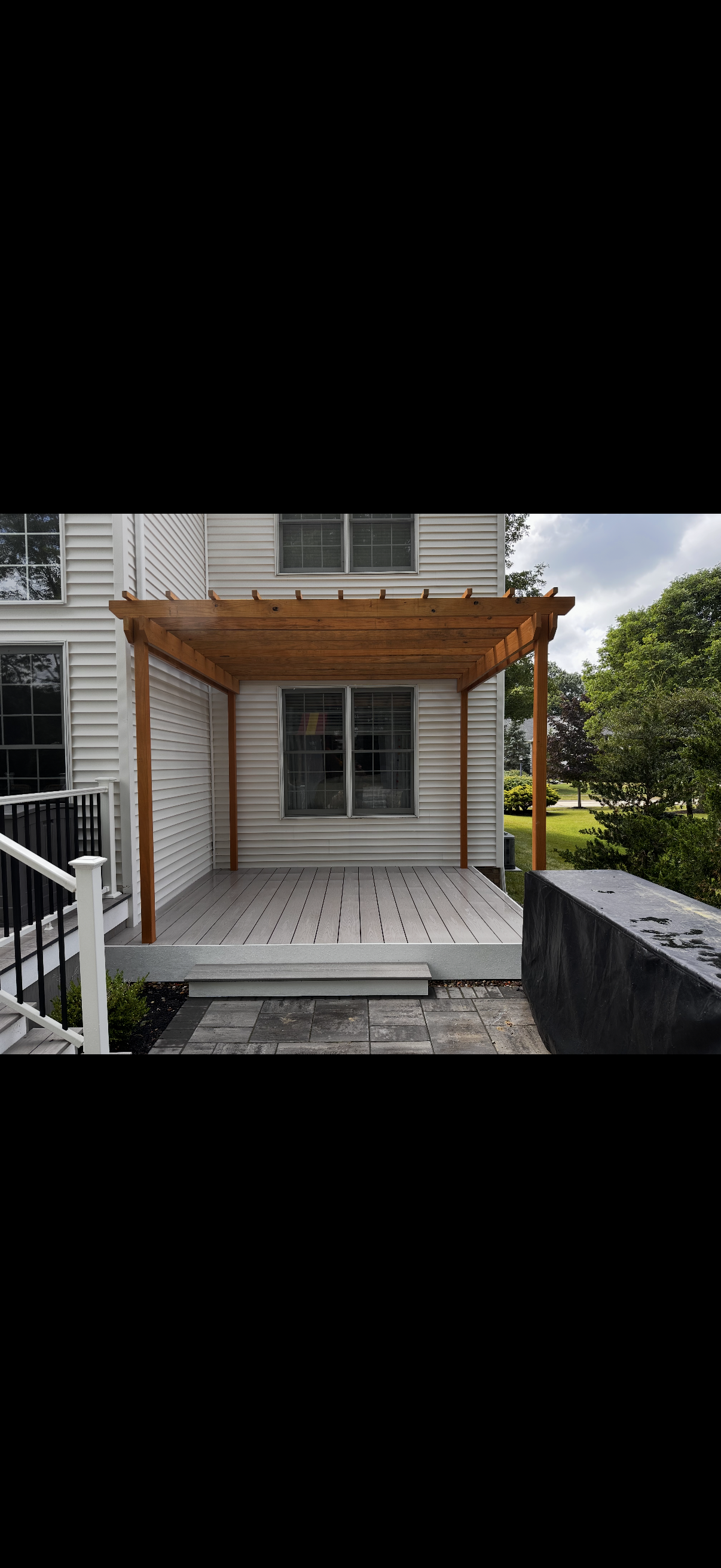 Covered front porch with wooden pergola, white siding, and steps leading to a house entrance