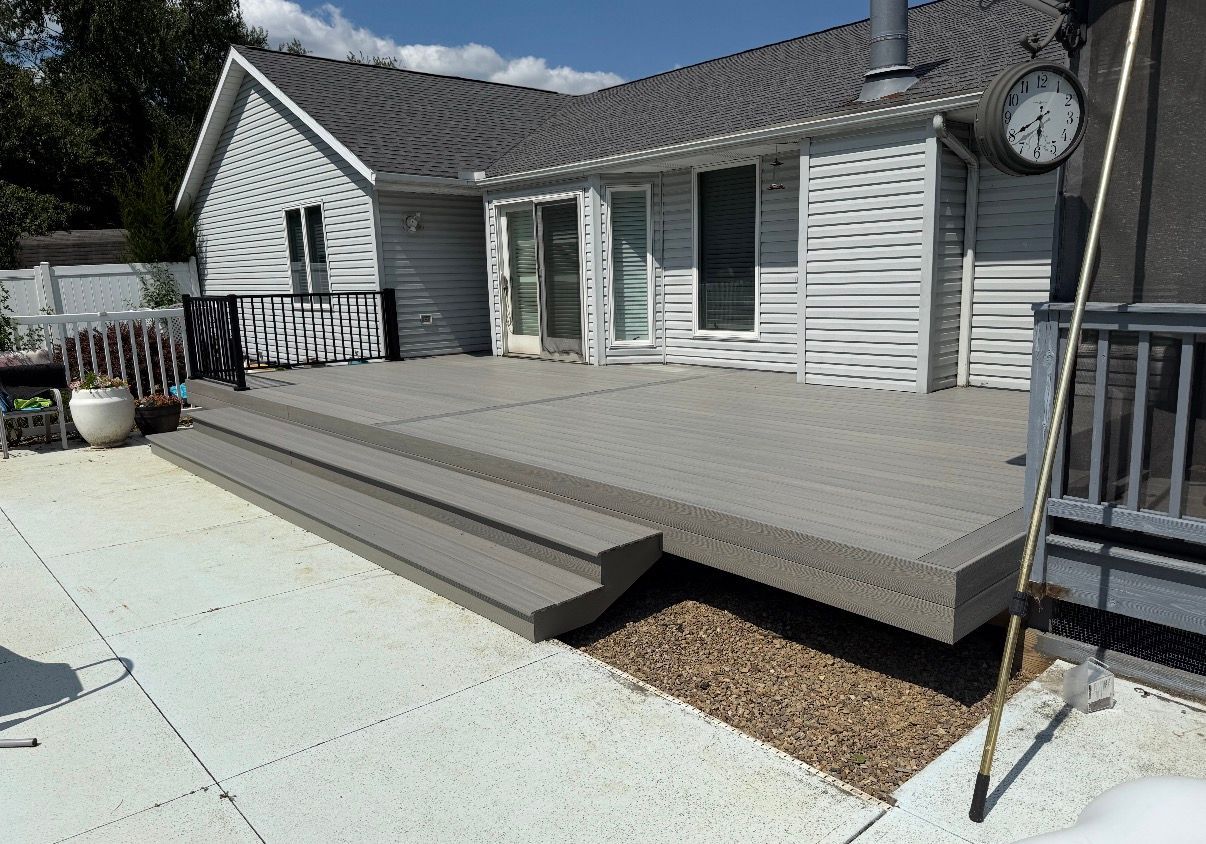 Gray wooden deck with steps beside a white house on a sunny day