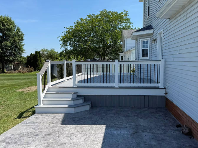 White backyard deck with steps, railing, and adjacent house beside a grassy lawn.