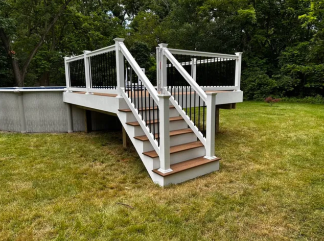White wooden deck stairs with railings leading to a raised patio in a grassy yard