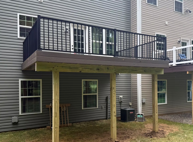 Raised wooden deck with black railing attached to a gray house exterior