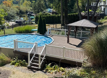 Backyard pool with a wooden deck, gazebo, and surrounding greenery on a sunny day