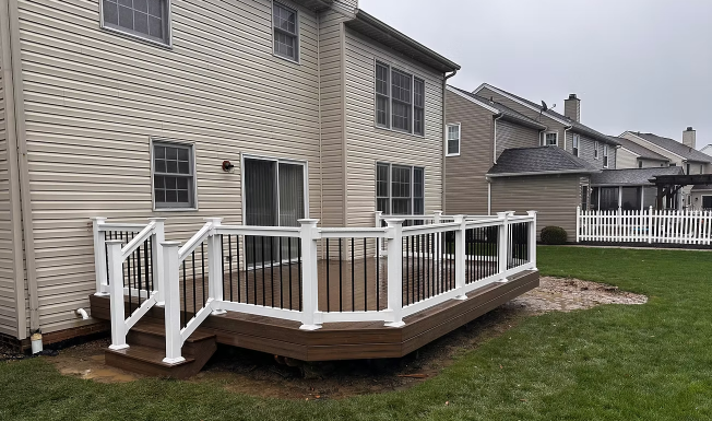Backyard wooden deck with white railings attached to a beige house in a suburban yard