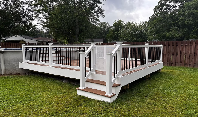 Wooden backyard deck with white railings and steps on a grassy lawn, under overcast skies