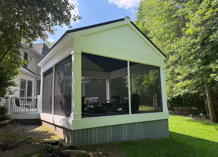 Screened porch extension on a house with white trim and green roof, surrounded by trees.