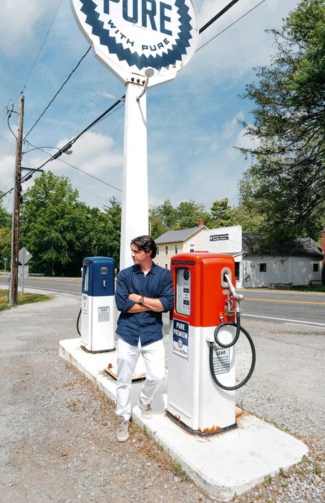 Person stands beside vintage blue and red gas pumps under a PURE sign.