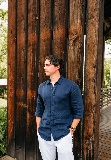 Man in a navy shirt standing beside a large weathered wooden wall outdoors.