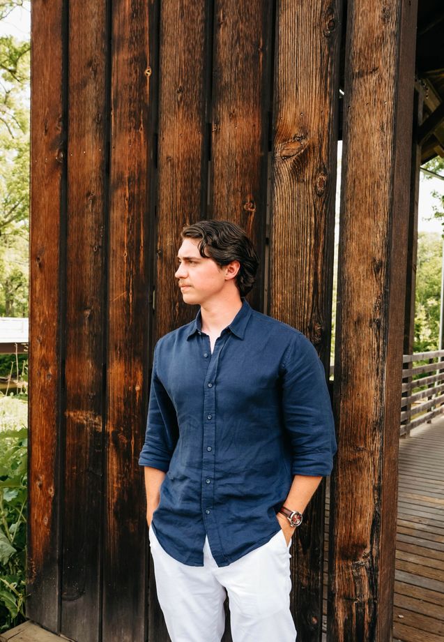 Man in a navy shirt standing beside a large weathered wooden wall outdoors.