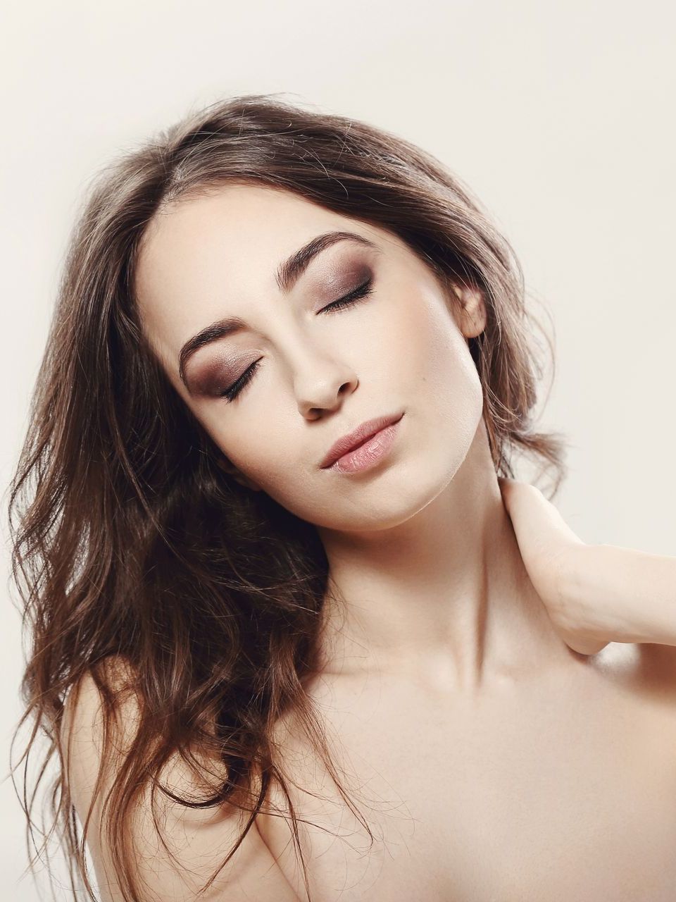 Woman with brown hair and closed eyes, hand on neck, wearing eye makeup.