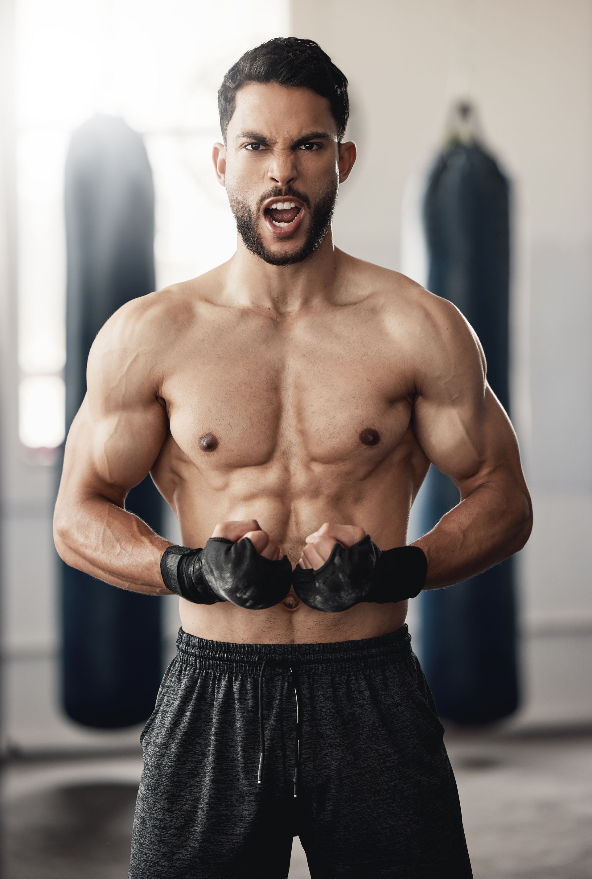 Fierce, muscular boxer in a gym, clenching fists, with an open mouth and angry expression.