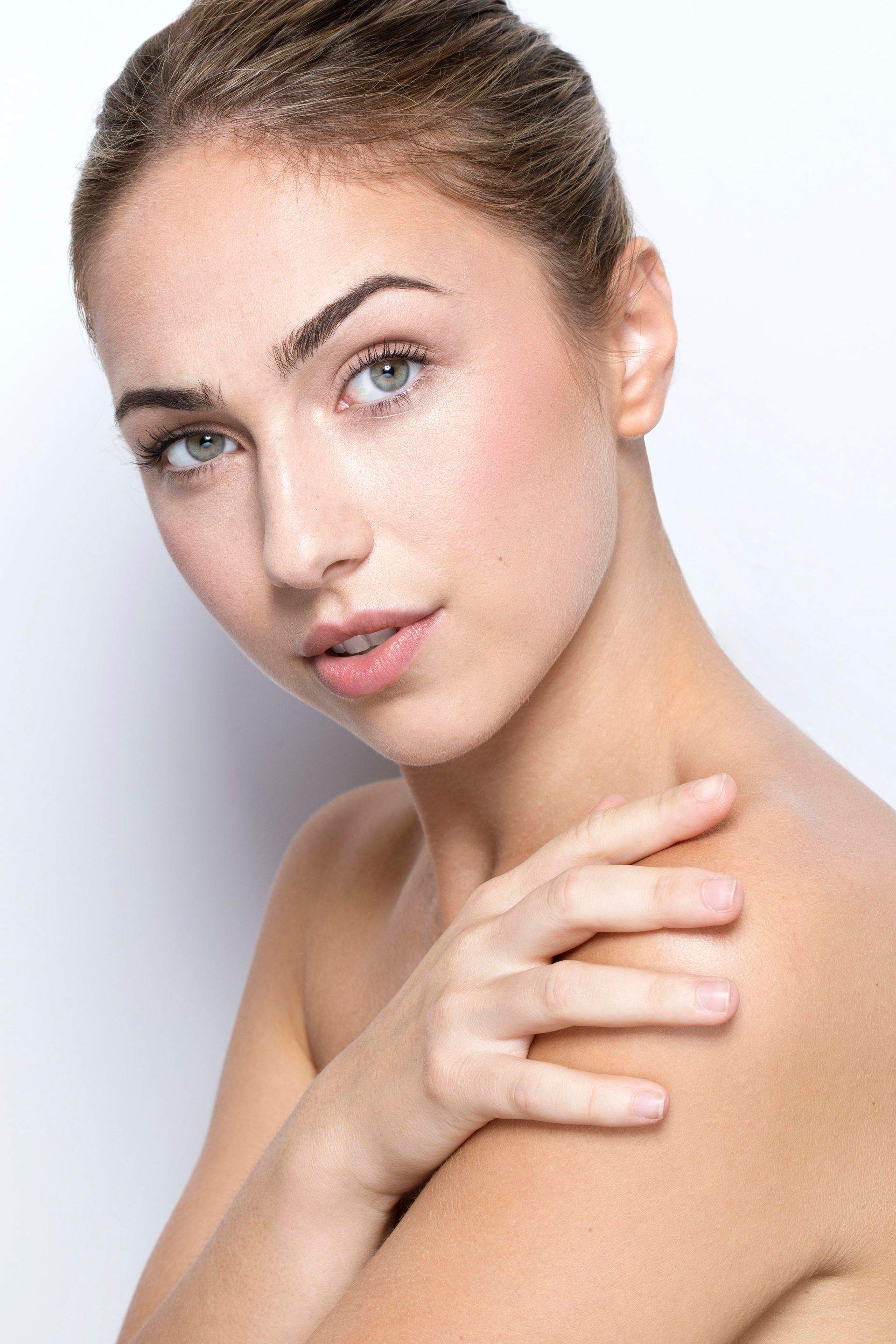 Woman with fair skin and light eyes, looking at the camera, hand on shoulder, against a white background.