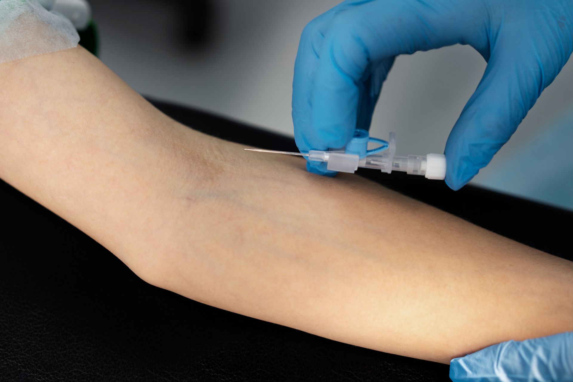 A gloved hand inserting an IV catheter into a person's arm.