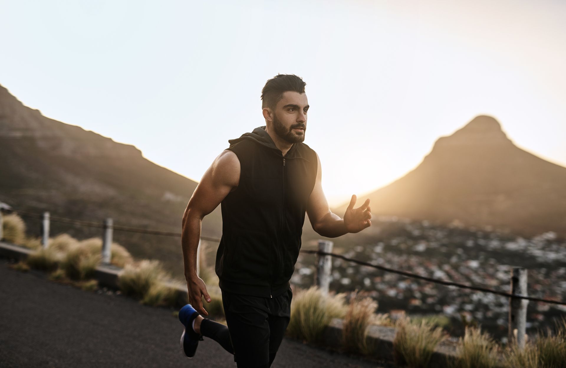 Man running uphill on a paved road, mountains and town in the background at sunset.