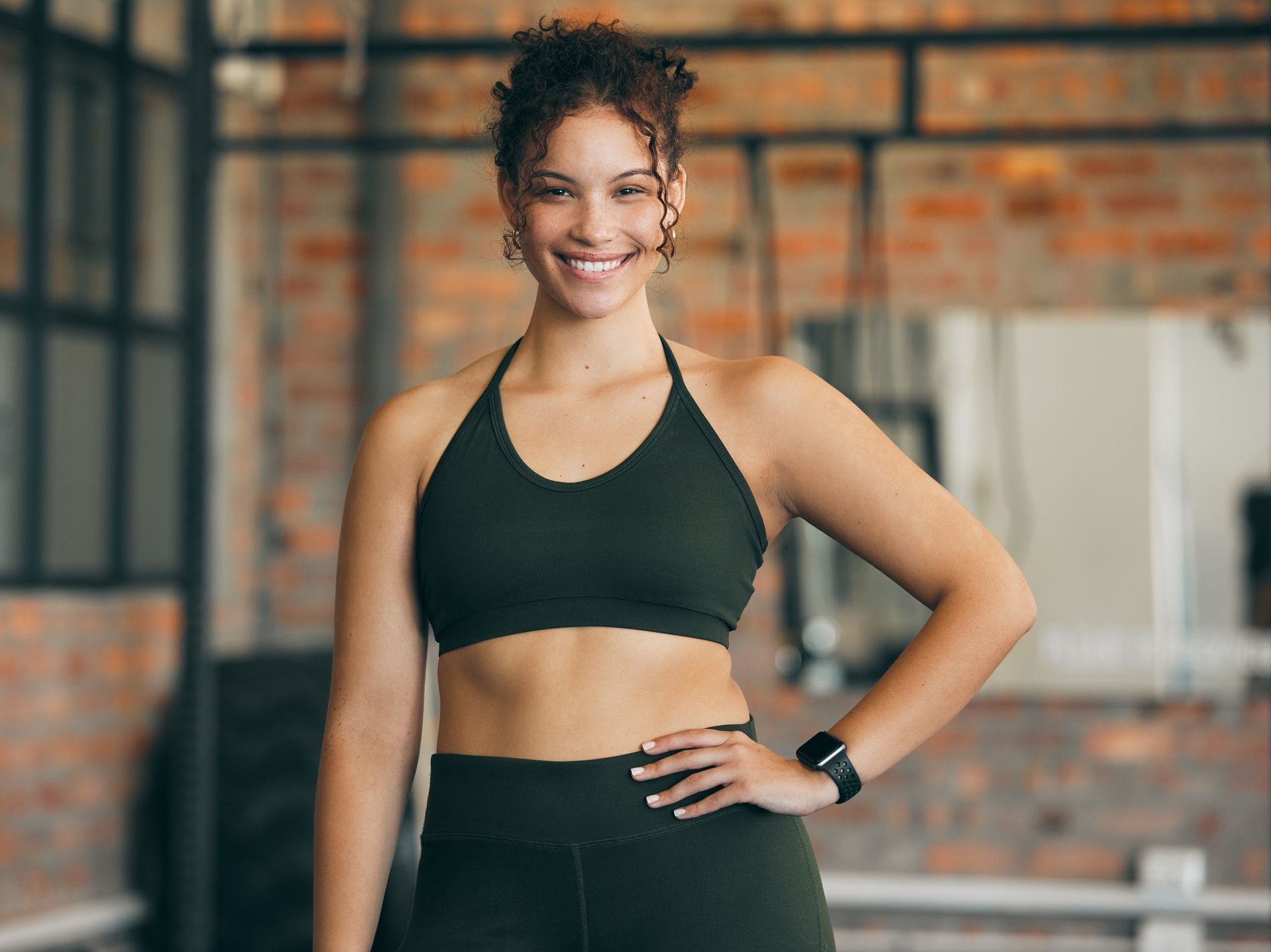 Woman in workout clothes, smiling, with hand on hip in gym.